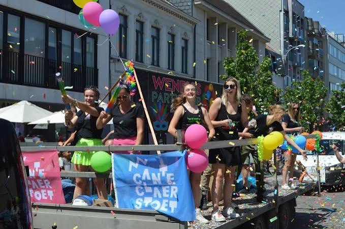 Deelnemers op een kleurrijk versierde wagen in de reclamestoet